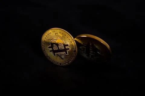 A low-key two physical golden Bitcoin token coins arranged over a solid bla.. Stock Photos