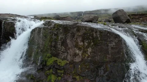 Low lateral drone flight past waterfall over large boulder, Reydarfjordur Stock Footage 346552246