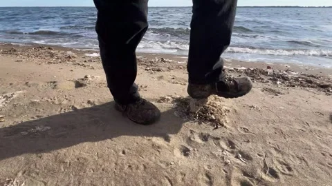 Low-level closeup of person walking on a beach near a wavy lake Video stock 273176536