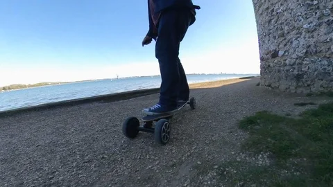Low level parallax shot of a man riding an electric skateboard on a gravel Stock Footage 107001955