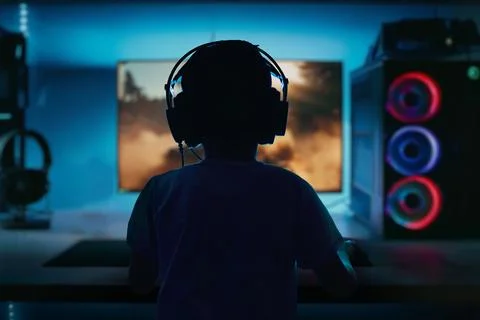 Low-light, high-contrast image of a boy playing a computer game on a gaming Stock Photos