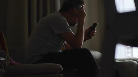 In a low-lit room, a man sits despondently on a couch, his face covered and.. Stock Footage 274473106