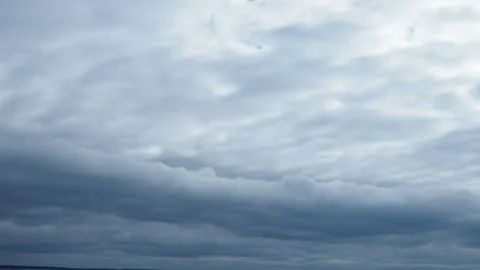 A low, long, heavy, oblong cloud floats across the sky above lake. Lighter white Vídeos de archivo 294666956