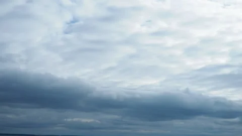 A low, long, heavy, oblong cloud floats across the sky above lake. Lighter white Vídeos de archivo 294678176