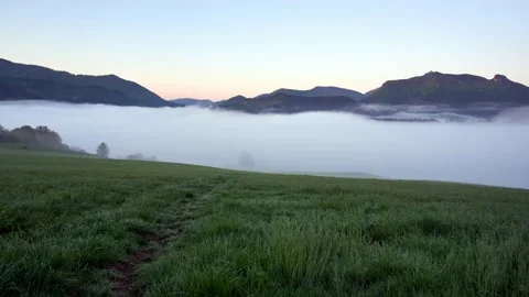Low mist clouds in the valley spill over into the countryside in the morning Stock Footage 195643304
