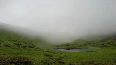 Low misty blue-gray clouds float quickly over the lake in the green hills Stock Footage 40618046