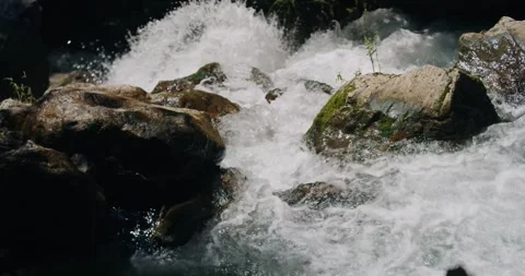 Low motion macro reveals exploding white foam surging over mossy boulders in Stock Footage 325506177