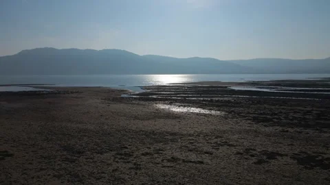 Low moving drone shot along a sandy beach as the sun reflects on the water Stock Footage 306470621
