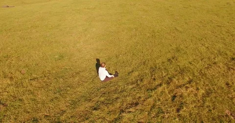 Low orbital flight around man on green grass with notebook pad at yellow rural Stock Footage 115085260