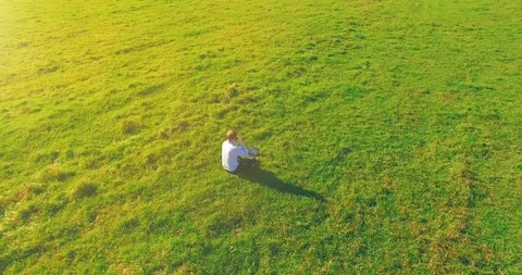 Low orbital flight around man on green grass with notebook pad at yellow rural Stock Footage 115085306