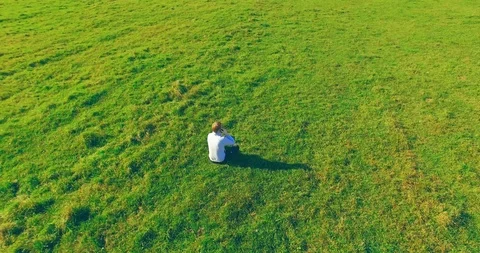 Low orbital flight around man on green grass with notebook pad at yellow rural Stock Footage 115085338