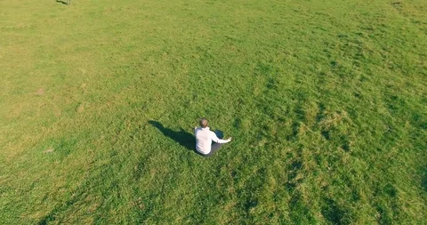 Low orbital flight around man on green grass with notebook pad at yellow rural Stock Footage 115085410