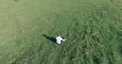 Low orbital flight around man on green grass with notebook pad at yellow rural Stock Footage 115085489