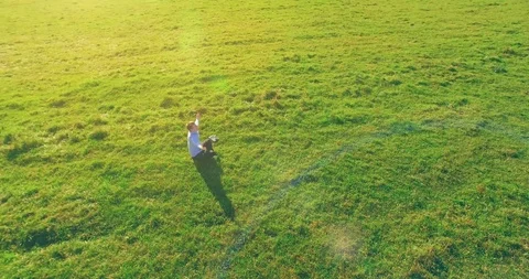 Low orbital flight around man on green grass with notebook pad at yellow rural Stock Footage 115085825