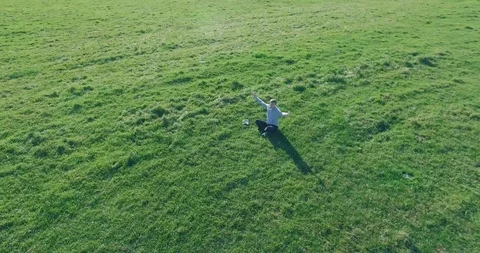 Low orbital flight around man on green grass with notebook pad at yellow rural Stock Footage 115086028