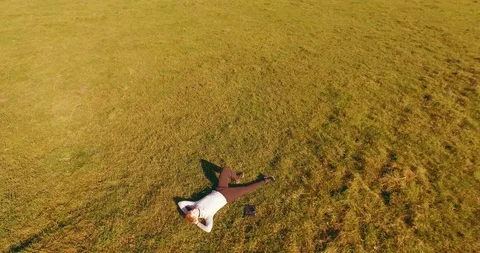 Low orbital flight around man on green grass with notebook pad at yellow rural Stock Footage 115086205