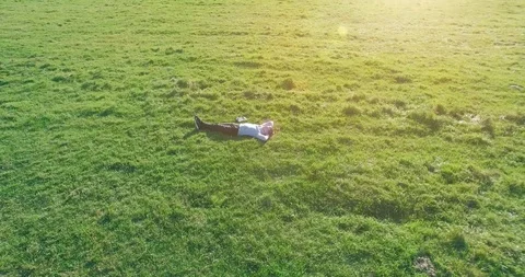 Low orbital flight around man on green grass with notebook pad at yellow rural Stock Footage 115086720