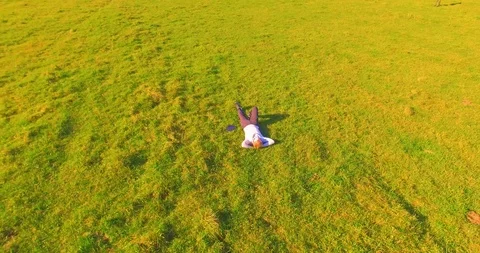 Low orbital flight around man on green grass with notebook pad at yellow rural Stock Footage 115086993