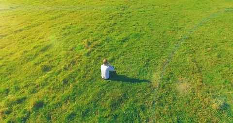 Low orbital flight around man on green grass with notebook pad at yellow rural Stock Footage 127337559
