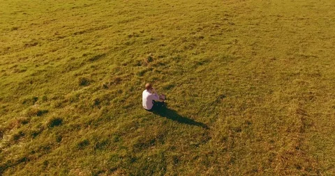 Low orbital flight around man on green grass with notebook pad at yellow rural Stock Footage 127337789