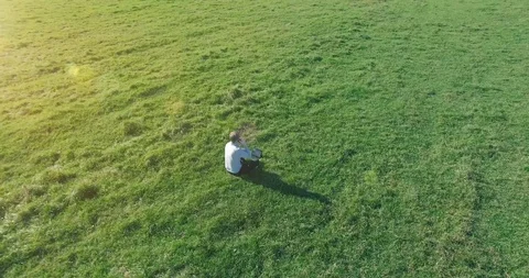 Low orbital flight around man on green grass with notebook pad at yellow rural Stock Footage 127338129