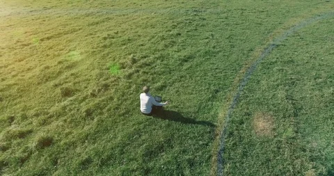 Low orbital flight around man on green grass with notebook pad at yellow rural Stock Footage 127338511