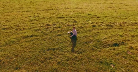 Low orbital flight around man on green grass with notebook pad at yellow rural Stock Footage 127338843
