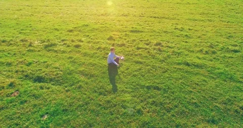 Low orbital flight around man on green grass with notebook pad at yellow rural Stock Footage 127339300