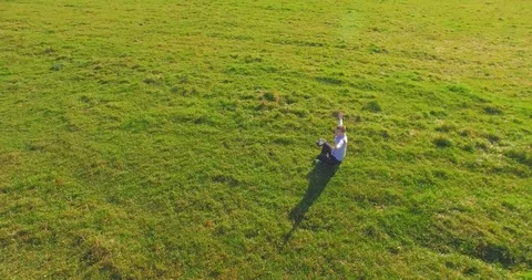 Low orbital flight around man on green grass with notebook pad at yellow rural Stock Footage 127340029
