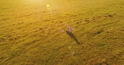Low orbital flight around man on green grass with notebook pad at yellow rural Stock Footage 127340429