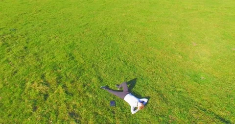 Low orbital flight around man on green grass with notebook pad at yellow rural Stock Footage 127340717
