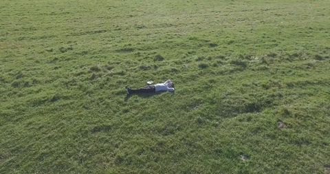 Low orbital flight around man on green grass with notebook pad at yellow rural Stock Footage 127341348