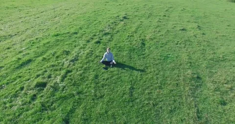 Low orbital flight around man on green grass with notebook pad at yellow rural Stock Footage 270008697