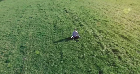 Low orbital flight around man on green grass with notebook pad at yellow rural Stock Footage 273659989