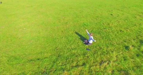 Low orbital flight around man on green grass with notebook pad at yellow rural Stock Footage 273660203