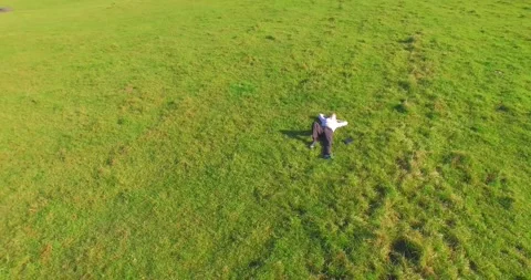 Low orbital flight around man on green grass with notebook pad at yellow rural Stock Footage 273660407