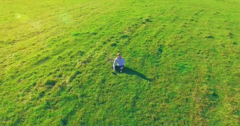 Low orbital flight around man on green grass with notebook pad at yellow rural Stock Footage 285432888