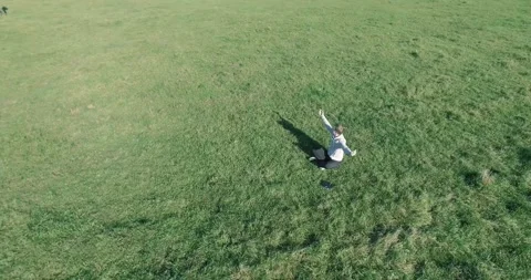 Low orbital flight around man on green grass with notebook pad at yellow rural Stock Footage 285477521