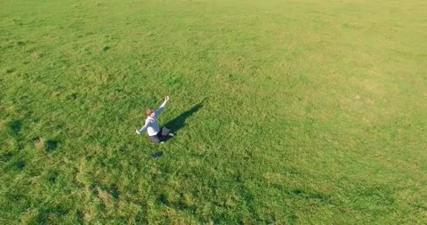 Low orbital flight around man on green grass with notebook pad at yellow rural Stock Footage 285477571