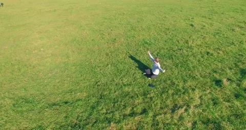 Low orbital flight around man on green grass with notebook pad at yellow rural Stock Footage 291782786