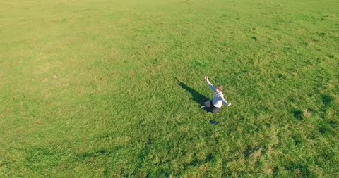 Low orbital flight around man on green grass with notebook pad at yellow rural Stock Footage 294421929
