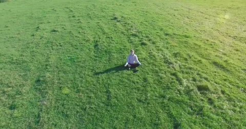 Low orbital flight around man on green grass with notebook pad at yellow rural Stock Footage 310717251