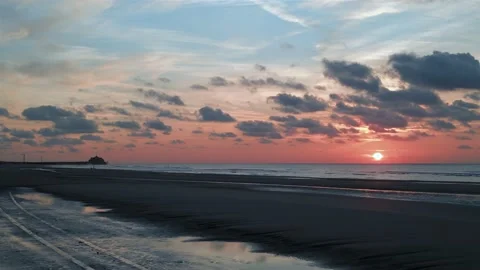 Low perspective aerial shot over dark beach at sunset with orange horizon 動画素材 220037846
