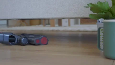 Low profile vacuum cleaner head cleaning hardwood floor surface under couch.. Vídeos de archivo 332882677
