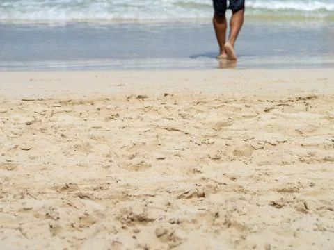 Low section of barefoot man walking into the waves on a sandy beach Stock Photos