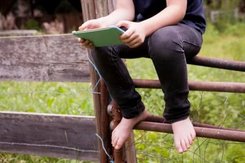 Low section of boy using tablet computer sitting on gate Foto stock