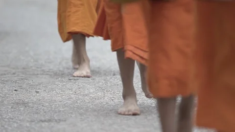 Low section of Buddhist monks wearing saffron robes while walking barefoot on Stock Footage 129110673