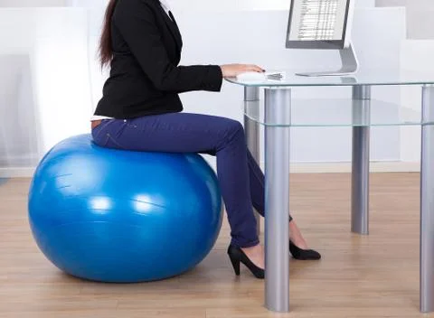 Low section of businesswoman using computer while sitting on pilates ball in  Foto stock