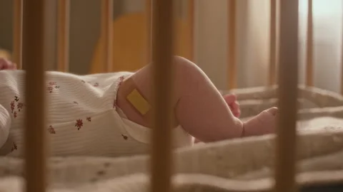 Low Section of Infant Baby with Patch on Leg Lying in Crib Stock Footage 335632218