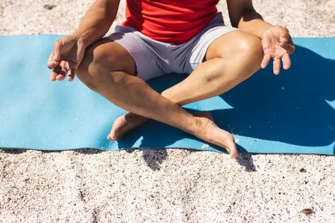 Low section of senior biracial man meditating in lotus position on yoga mat Stock Photos